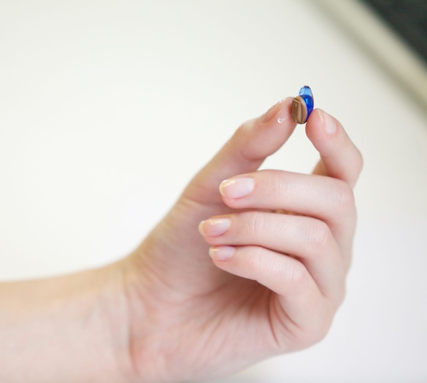 A tiny compact hearing aid held between two fingers